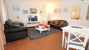 A living room with a sofa, a coffee table, a TV, and a dining table with chairs.