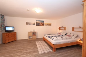 Un dormitorio con una cama de madera, un aparador de madera, un televisor y estantes en la pared.