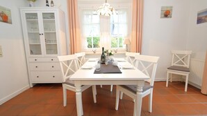 A dining area with a white table set for four, a cabinet with glass doors, and a window with curtains.