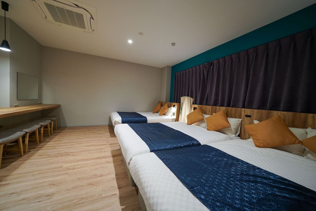 A hotel room with two beds, a desk with chairs, and a large window with curtains.