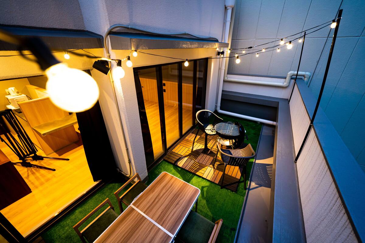 A compact outdoor patio with a table and chairs, string lights, and a small garden area.