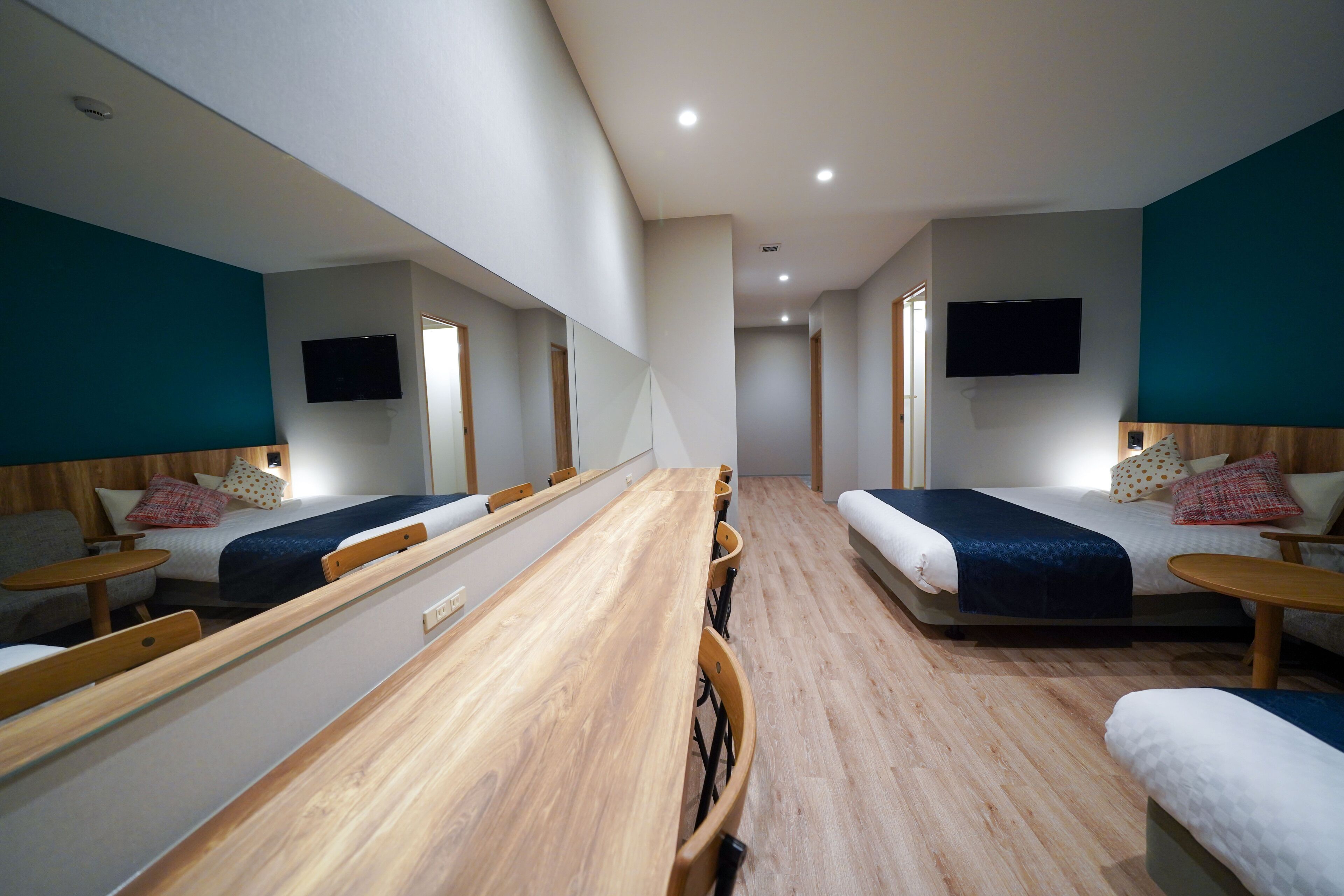Una habitación de hotel con dos camas, una mesa de madera y un televisor montado en la pared.