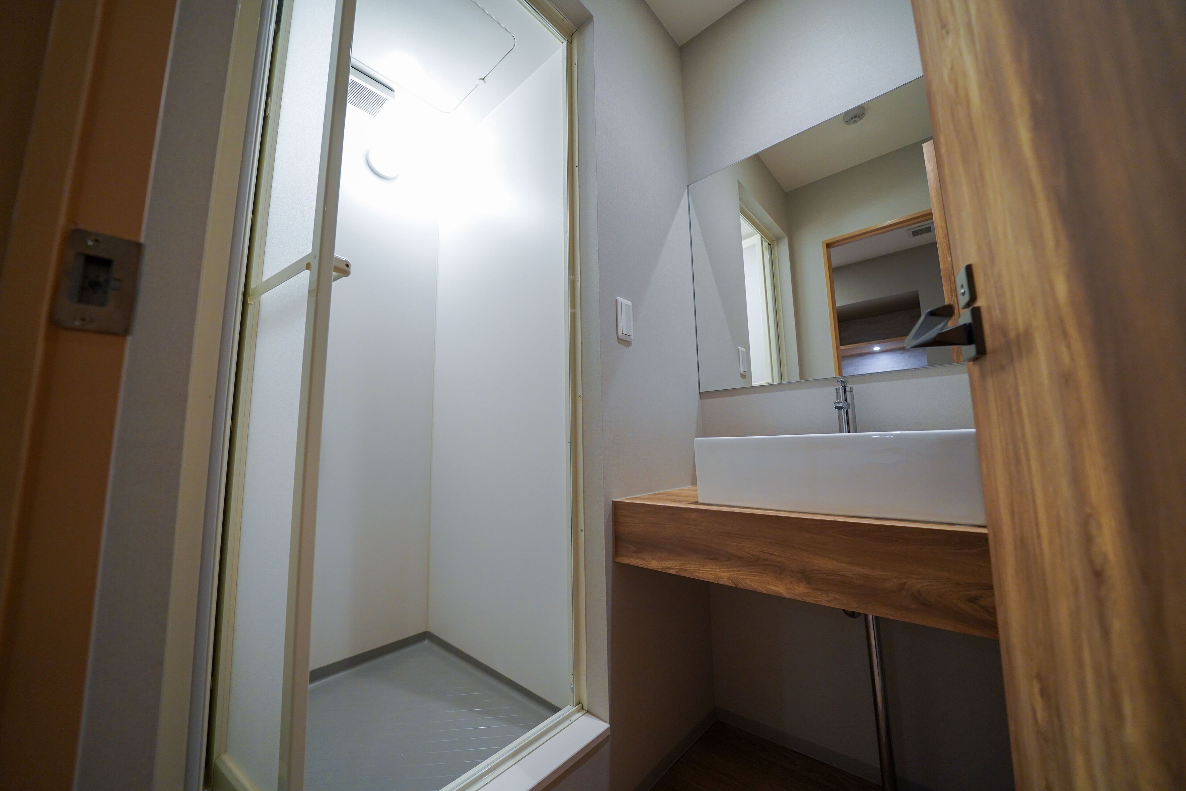 Een badkamer met een houten wastafelmeubel, een spiegel en een douchehoek.