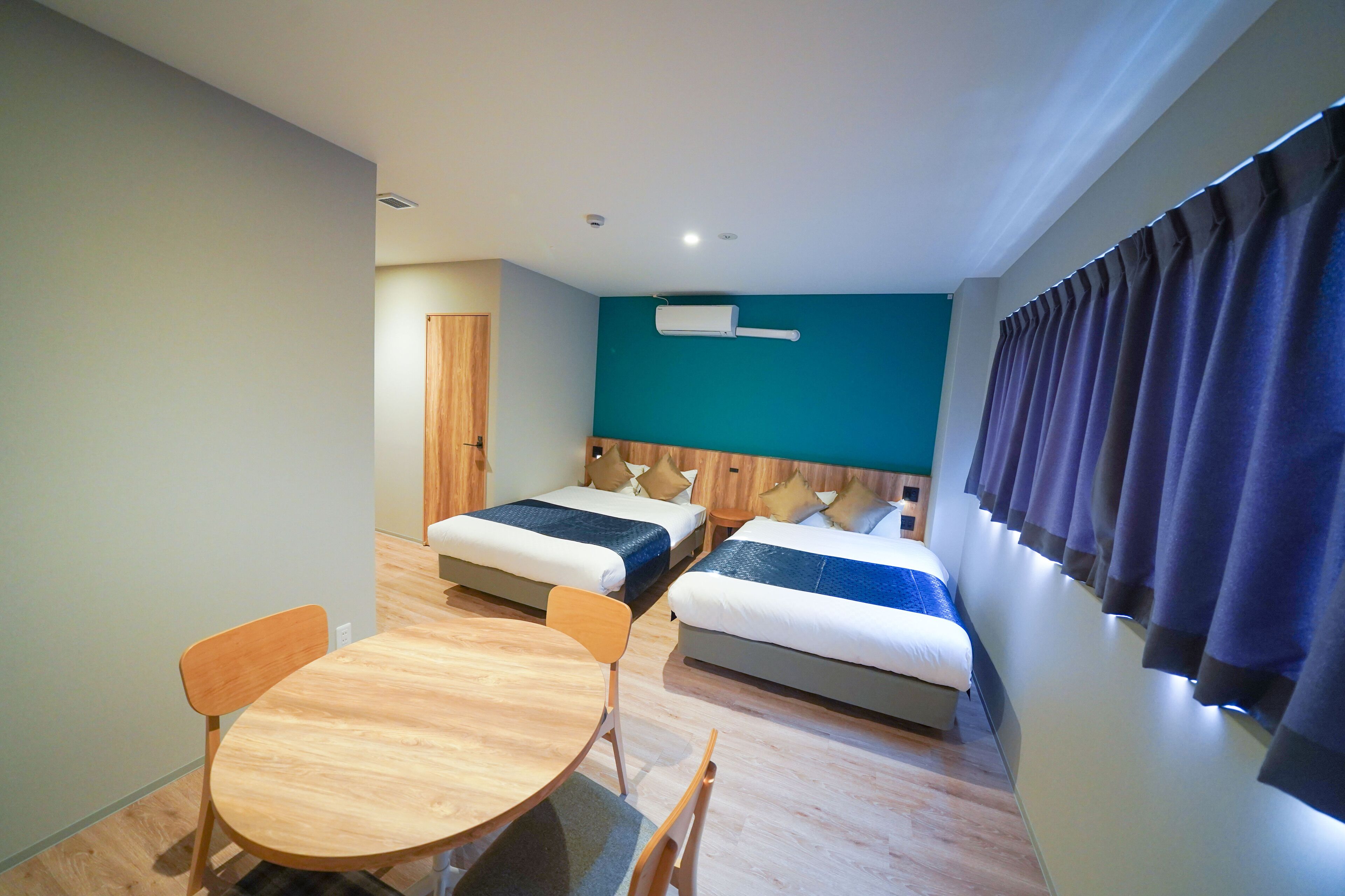 A hotel room with two beds, a wooden table, and a window with curtains.