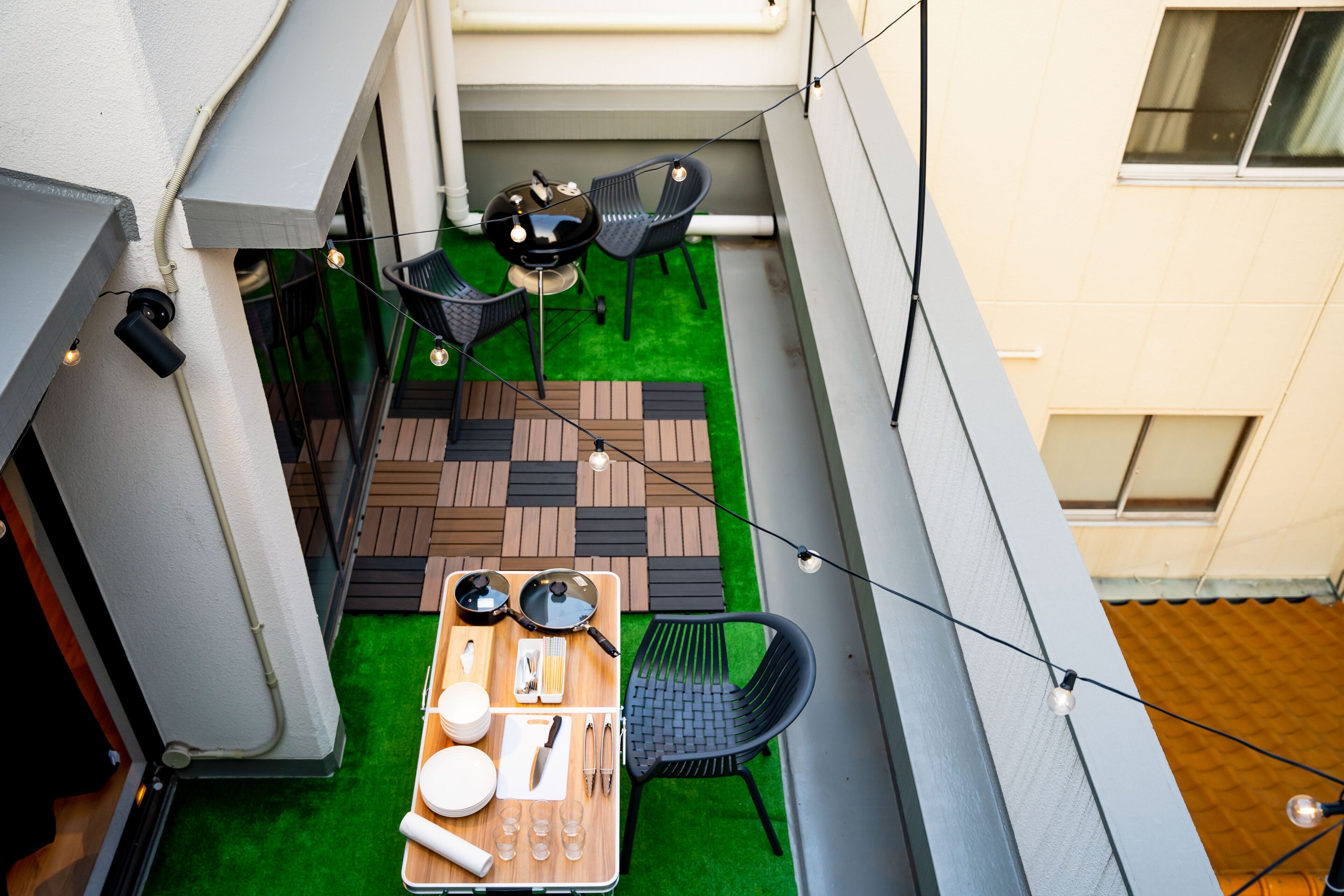 A rooftop terrace with a wooden table set for dining, two black chairs, and a small grill.