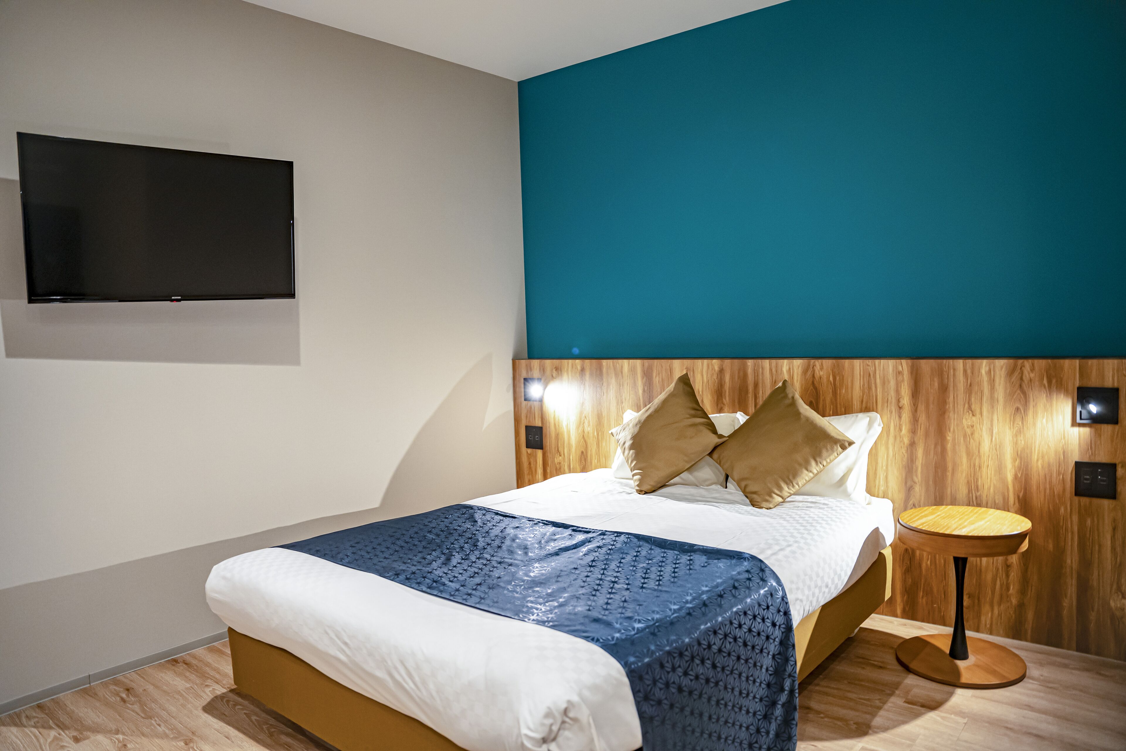 Een moderne hotelkamer met een bed, een aan de muur bevestigde televisie en een klein rond tafeltje.