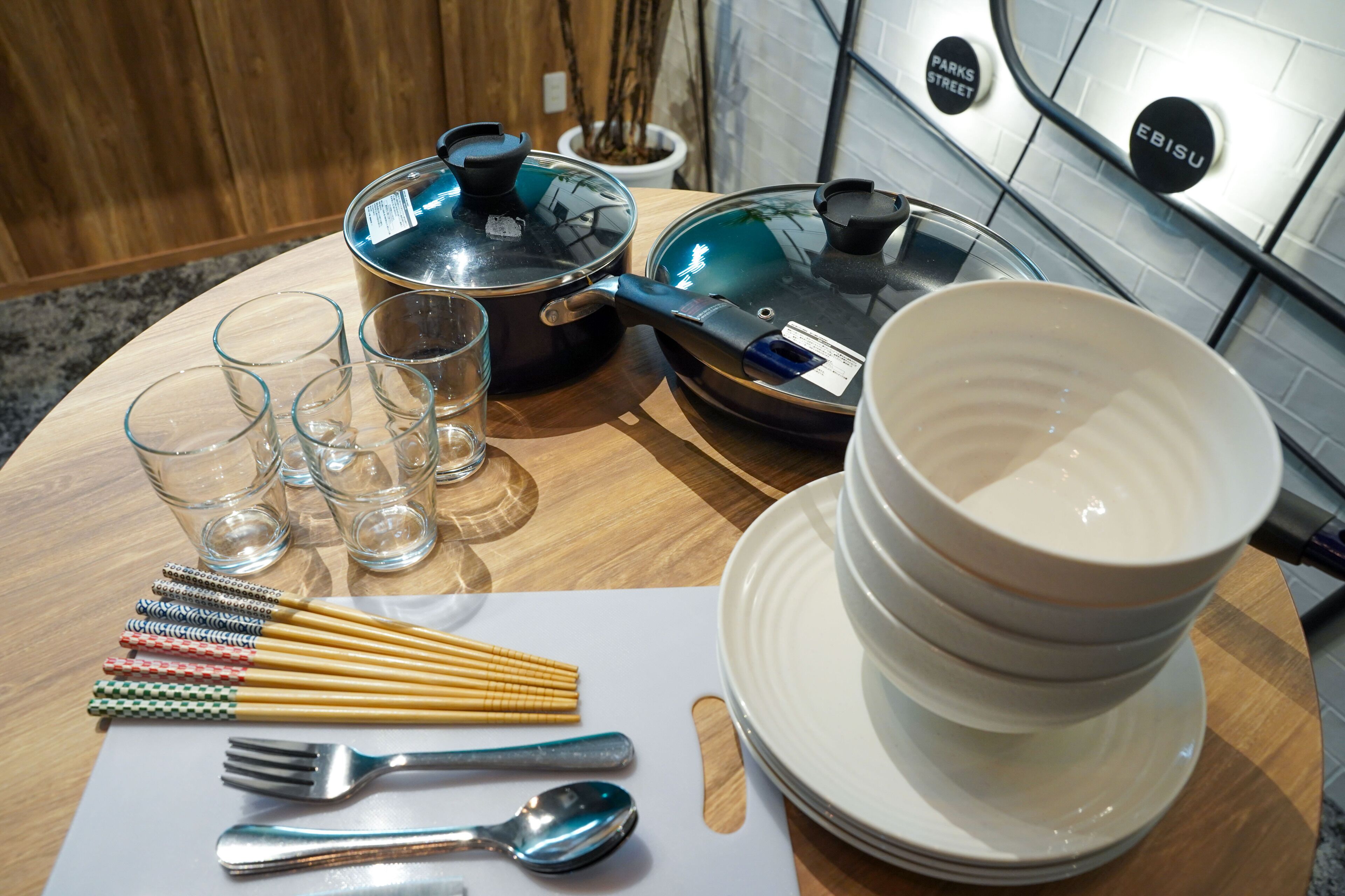 A kitchen counter with a pot, a pan, a stack of bowls, chopsticks, a fork, and a spoon.