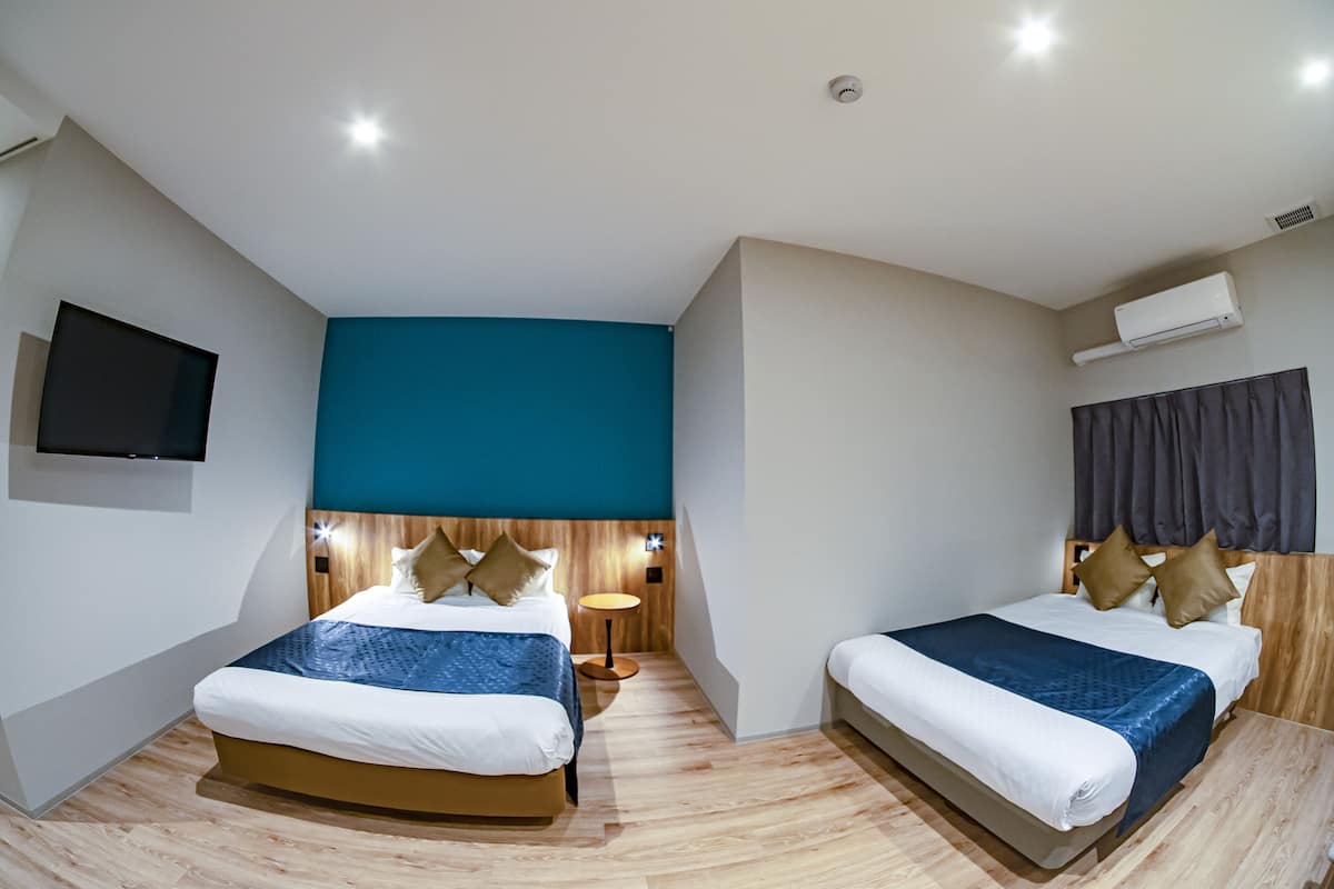 A modern hotel room with two beds, a TV, a small round table, and an air conditioning unit.