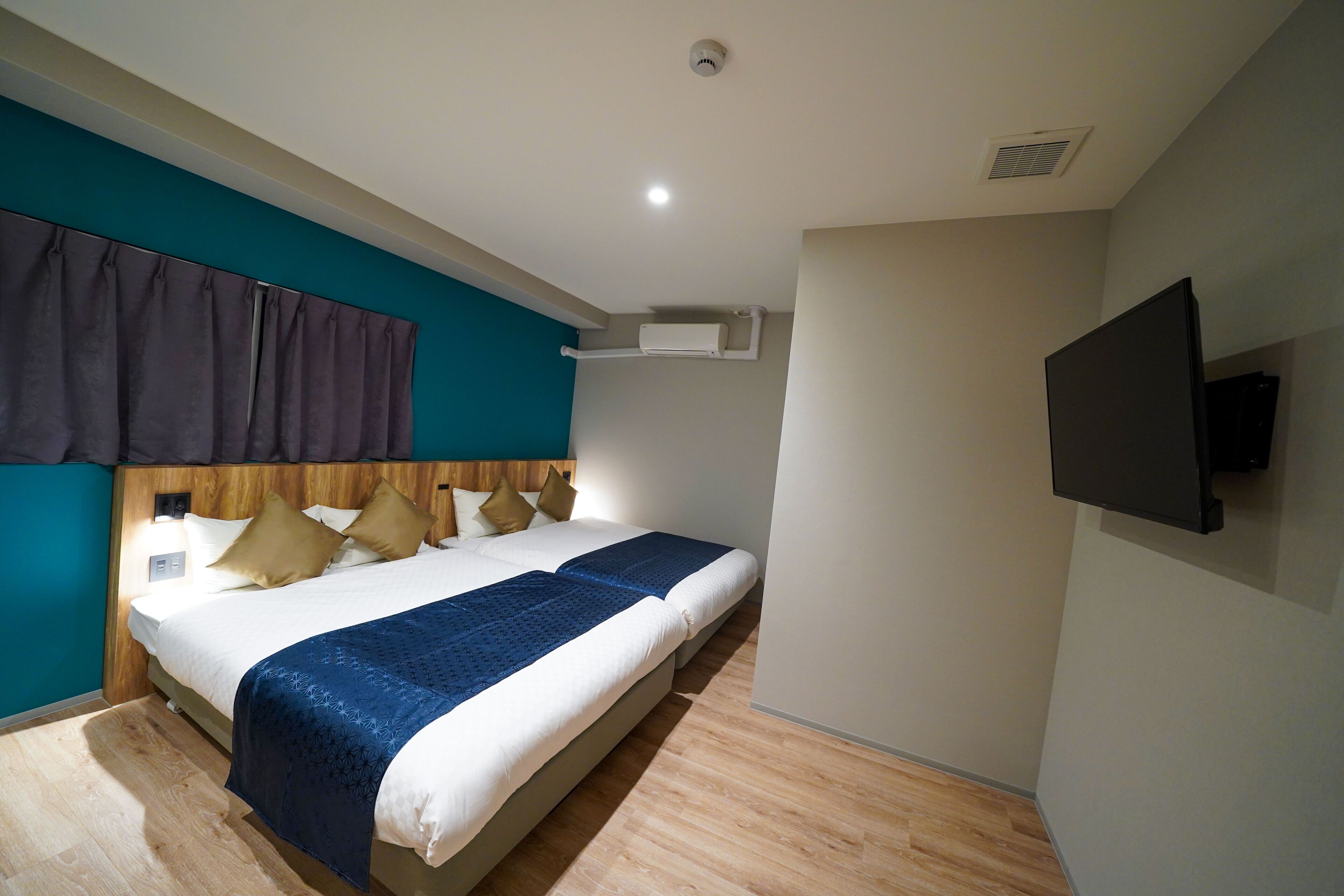 Une chambre d’hôtel avec un lit, un téléviseur fixé au mur et une bouche d’aération au plafond.