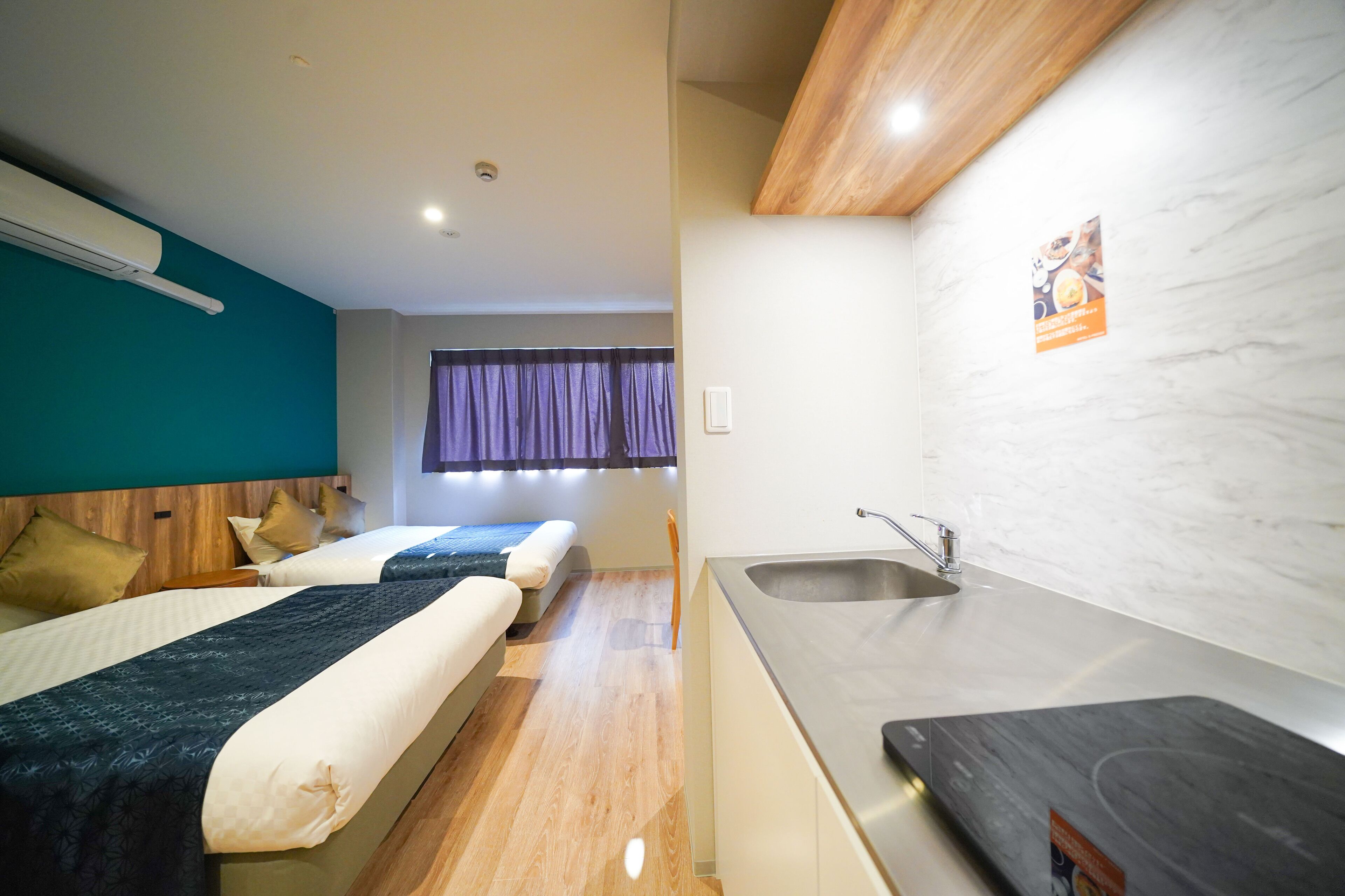 A hotel room with two beds, a kitchenette, and a bathroom with a shower.