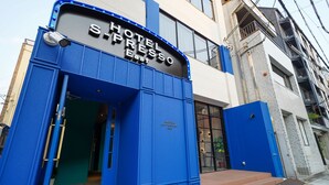 Entrada de hotel com fachada azul e uma placa com a inscrição "HOTEL S-Presso East".
