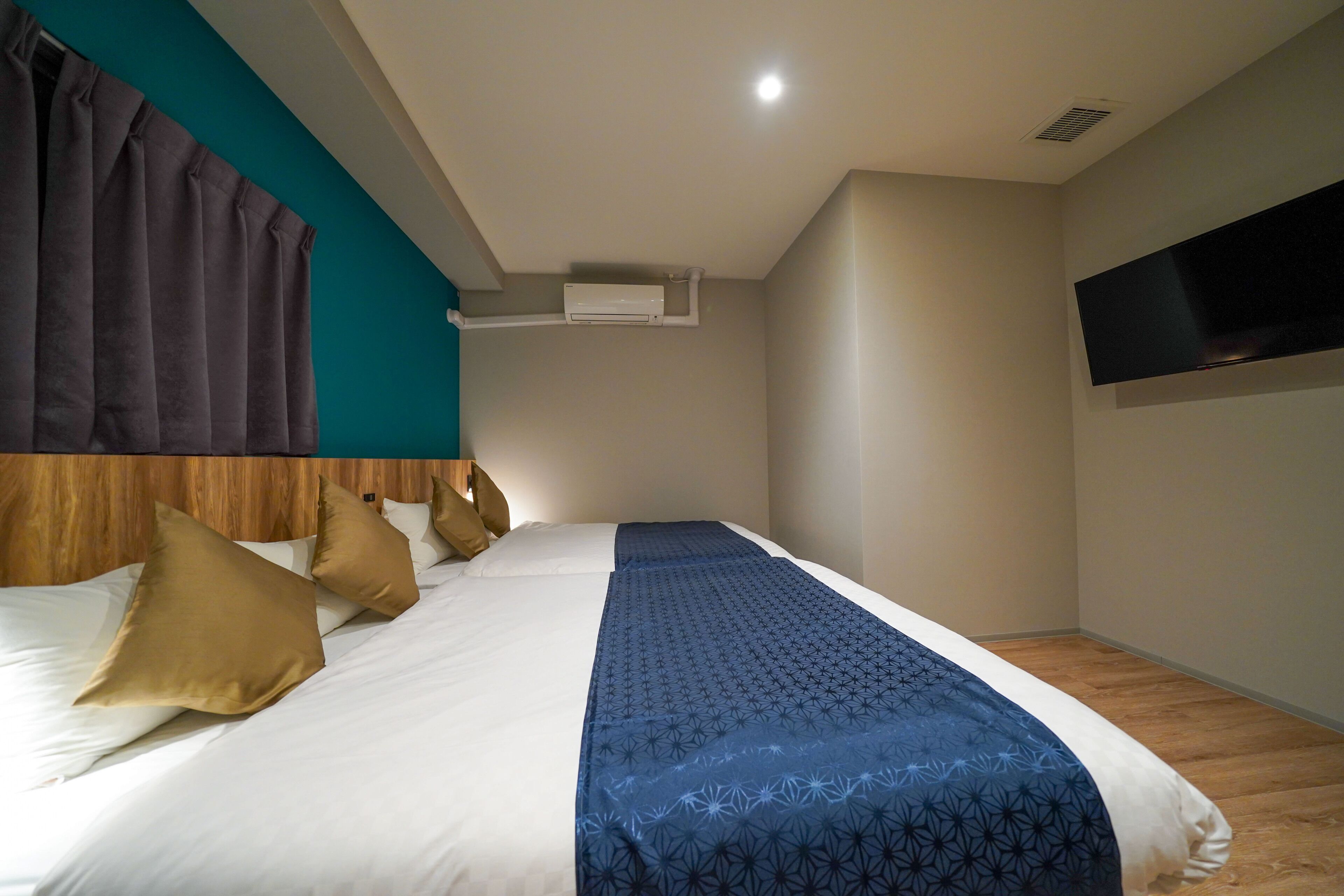 Habitación de hotel con cama, televisor montado en la pared y aire acondicionado instalado en el techo.