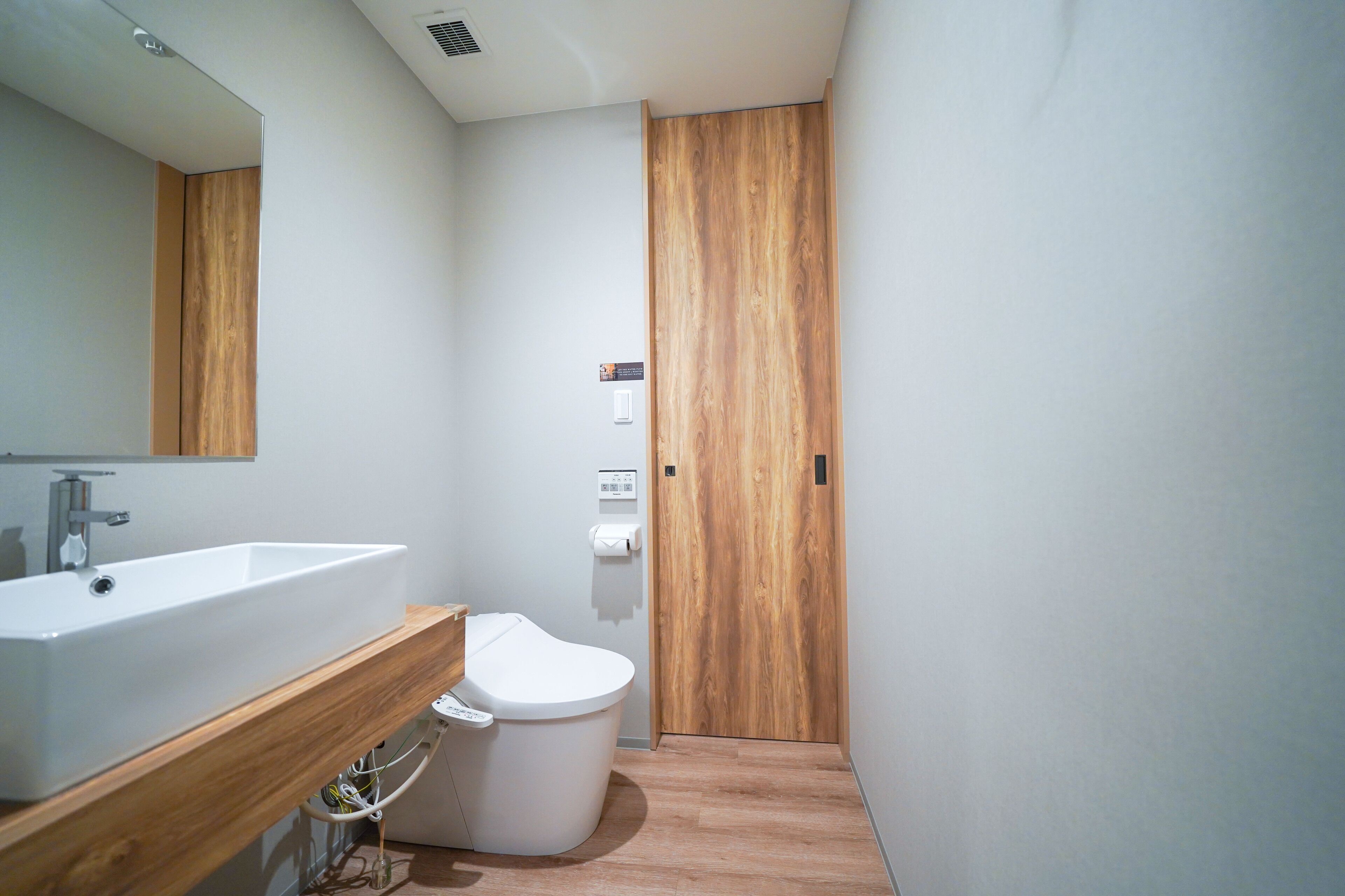 A modern bathroom with a wooden vanity, white sink, and toilet.