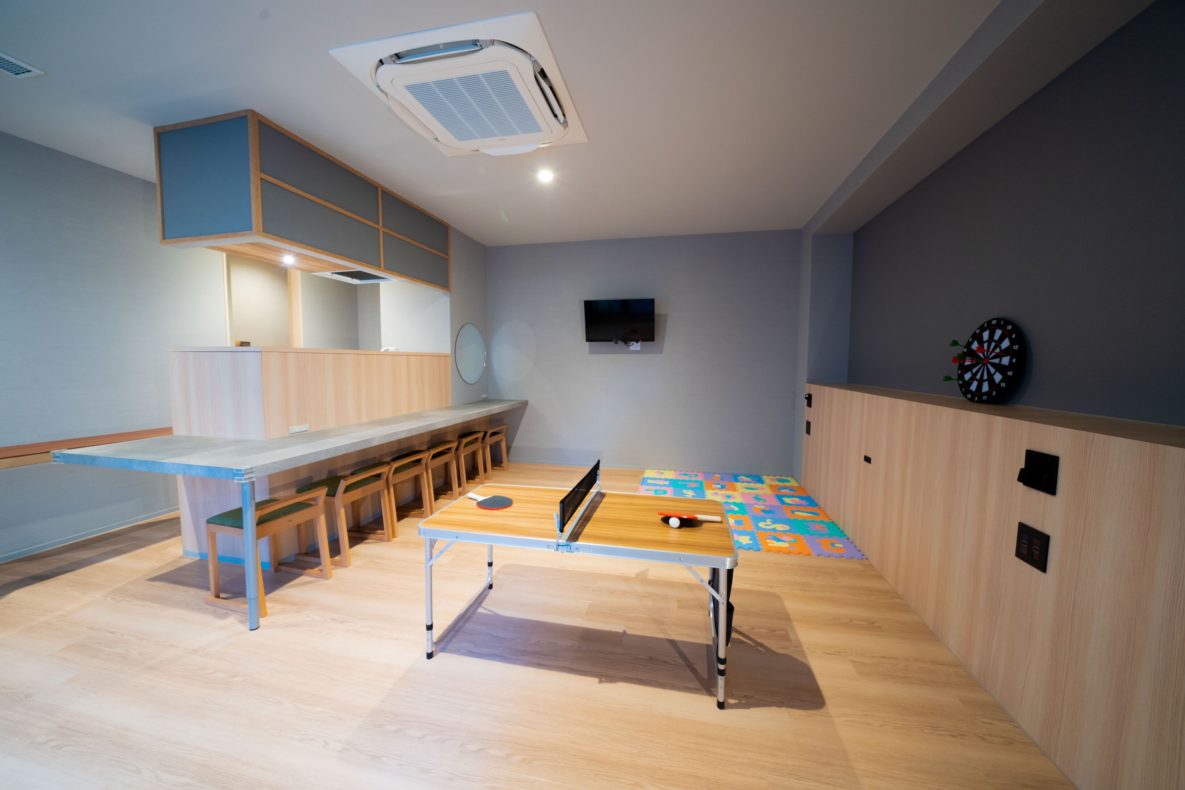 A room with a ping pong table, a dartboard, and a television on the wall.