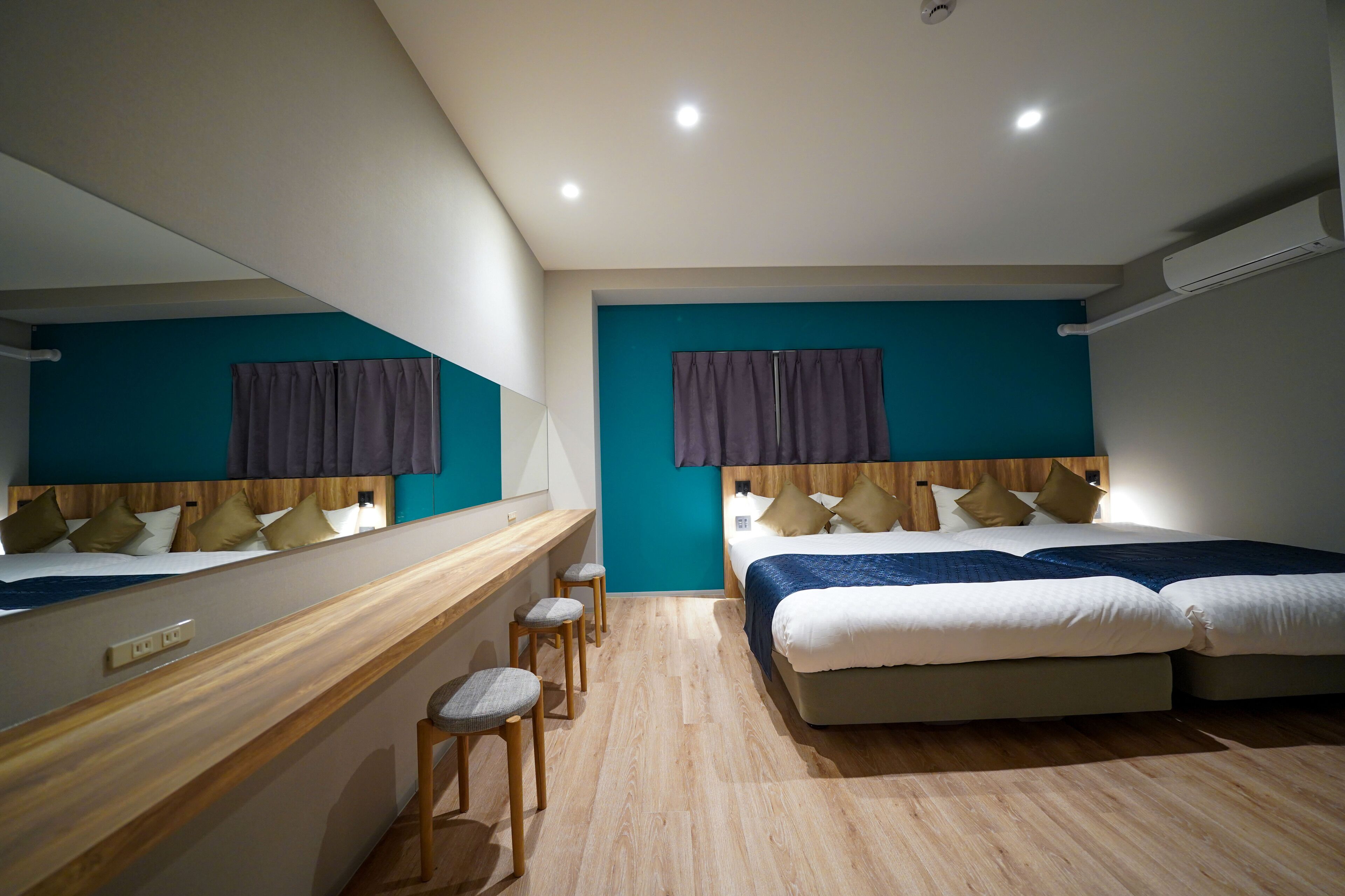 A modern hotel room with two beds, a wooden desk, and a large mirror.