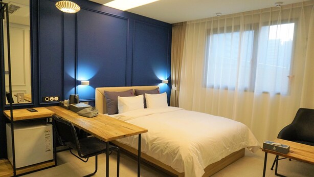 A hotel room with a bed, desk, chair, and a small kitchenette. - Yeoubi Hotel (Changwon)