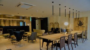 A modern hotel lobby with a long wooden table and multiple chairs, a reception desk, and a wall-mounted logo. - Yeoubi Hotel (Changwon)