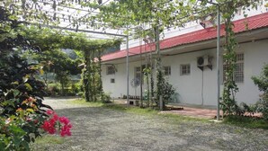 Un edificio con tejado de tejas rojas, un patio de grava y una pérgola cubierta de plantas trepadoras.