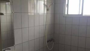 Un baño pequeño y limpio con azulejos blancos, inodoro, lavamanos y ducha.
