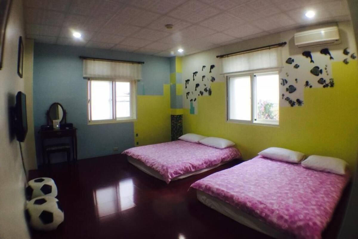 Habitación con dos camas, una ventana y una pared decorada con calcomanías de peces.