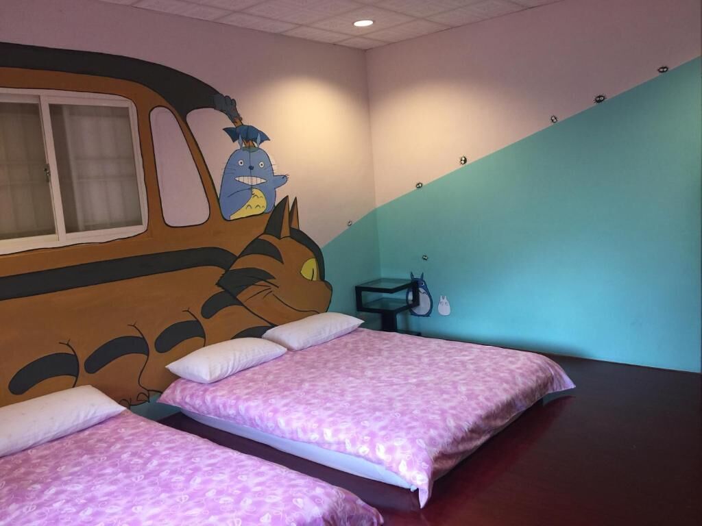 A room with two beds, a wall mural of a cartoon character, a small table, and a window.