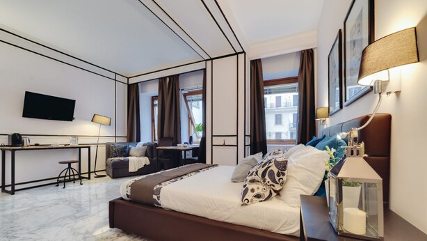 A modern hotel room with a large bed, a desk, a TV, and a view of the city.