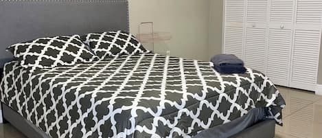 A bed with a patterned bedspread, a grey headboard, and a metal storage unit against the wall.