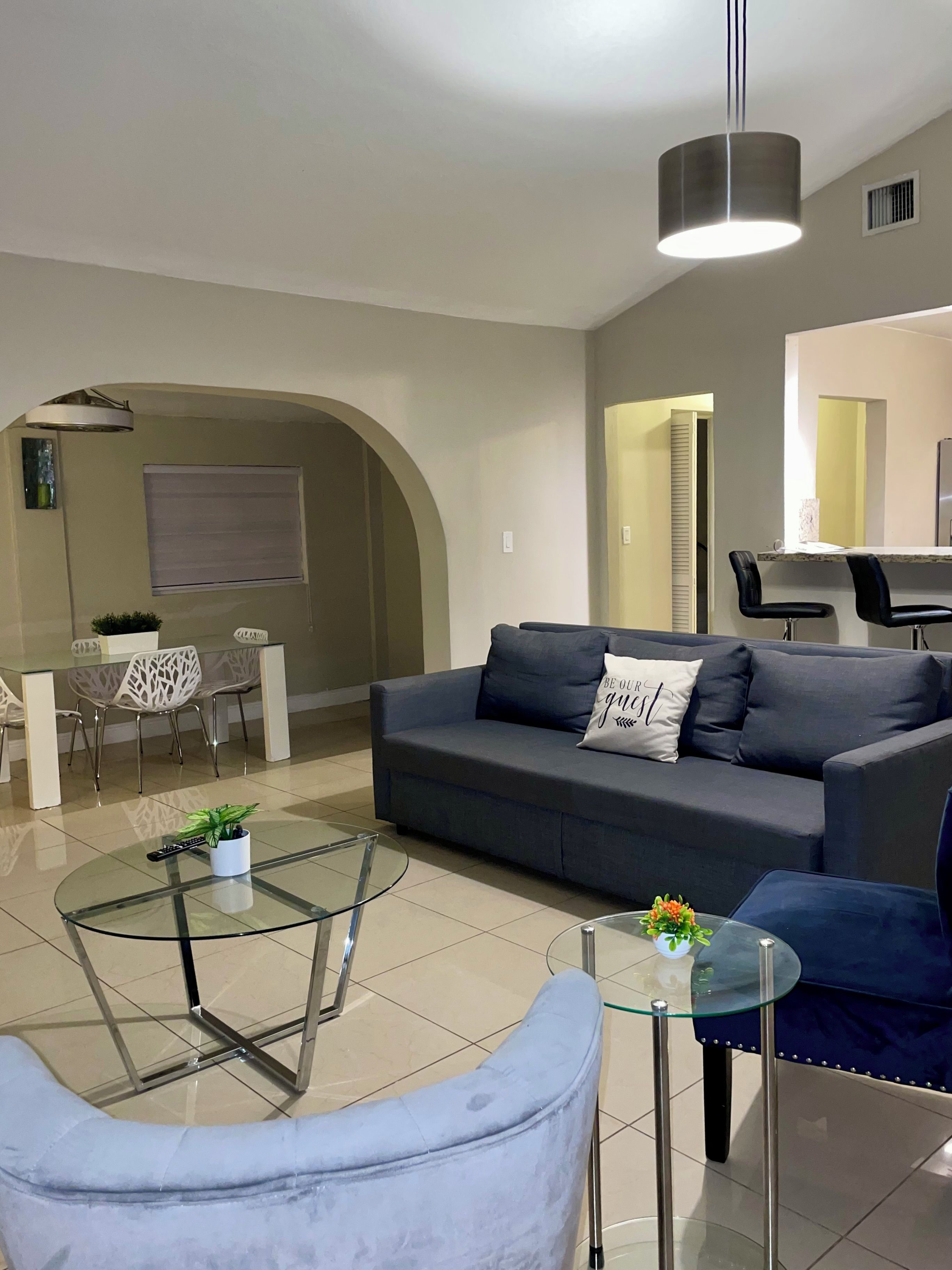 A modern living room with a sofa, a glass coffee table, and a dining area with chairs and a table.