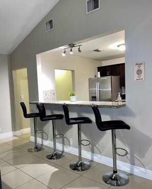 A modern kitchen with a bar area, stainless steel appliances, and a 'Welcome!' sign.