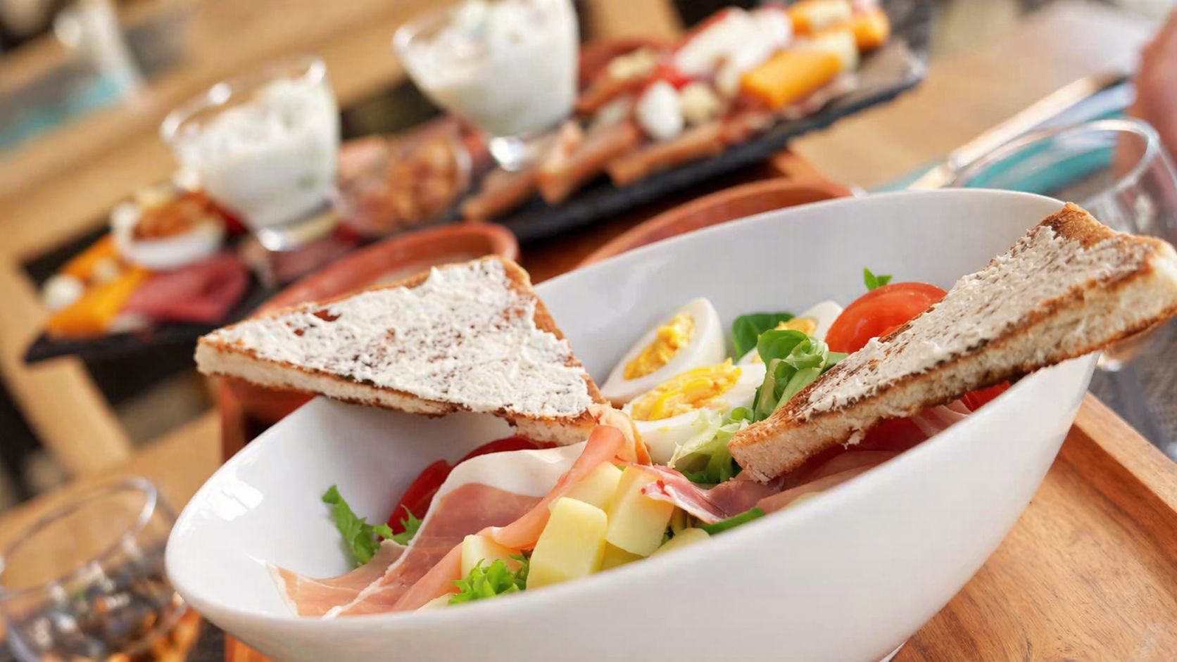 A white bowl containing a salad with bread, eggs, and meat.