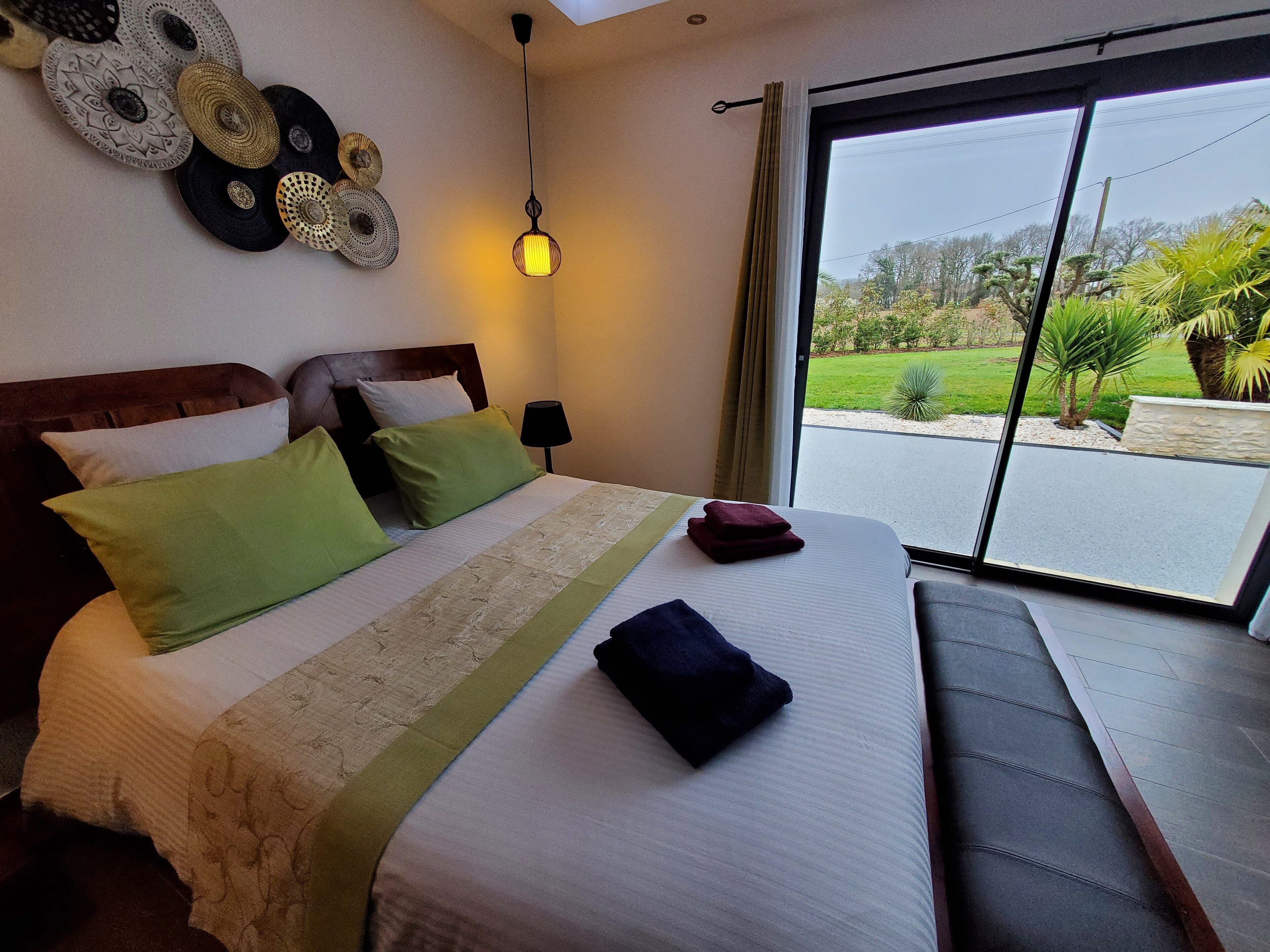 Habitación de hotel con cama, almohadas, lámpara de noche, vistas al exterior e iluminación en el techo.