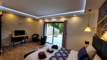 Un dormitorio moderno con una cama grande, un escritorio y una silla. Se ve un jardín a través de la puerta de vidrio.