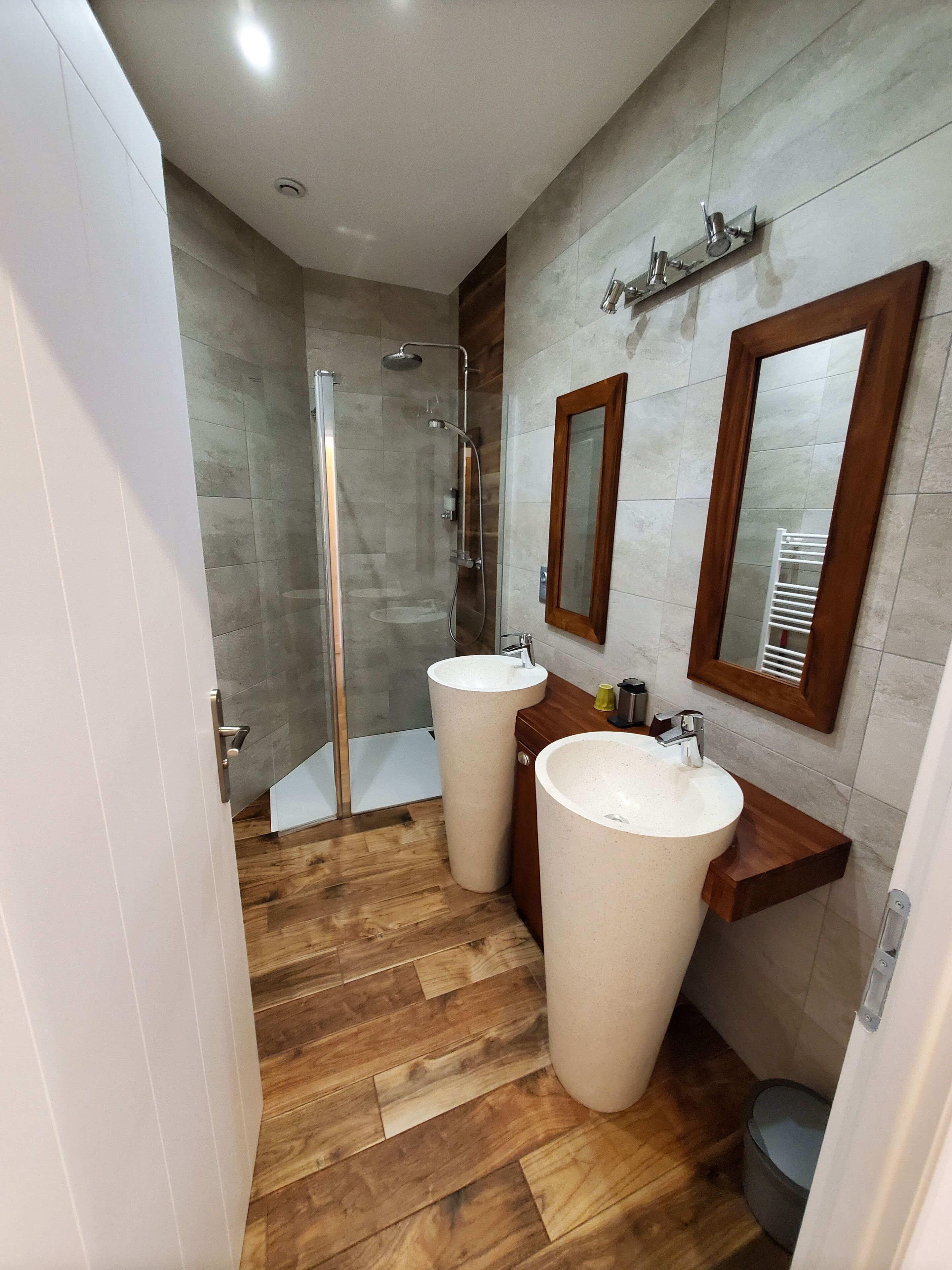 Ein modernes Badezimmer mit zwei Waschbecken, einer Dusche und Holzboden.