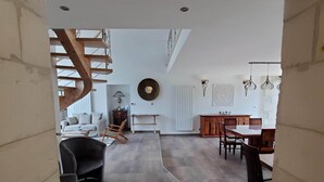 A spacious living area with a wooden staircase, a dining table with chairs, and a kitchen area with a white countertop and cabinets. - Les Cuves (Chaniers)