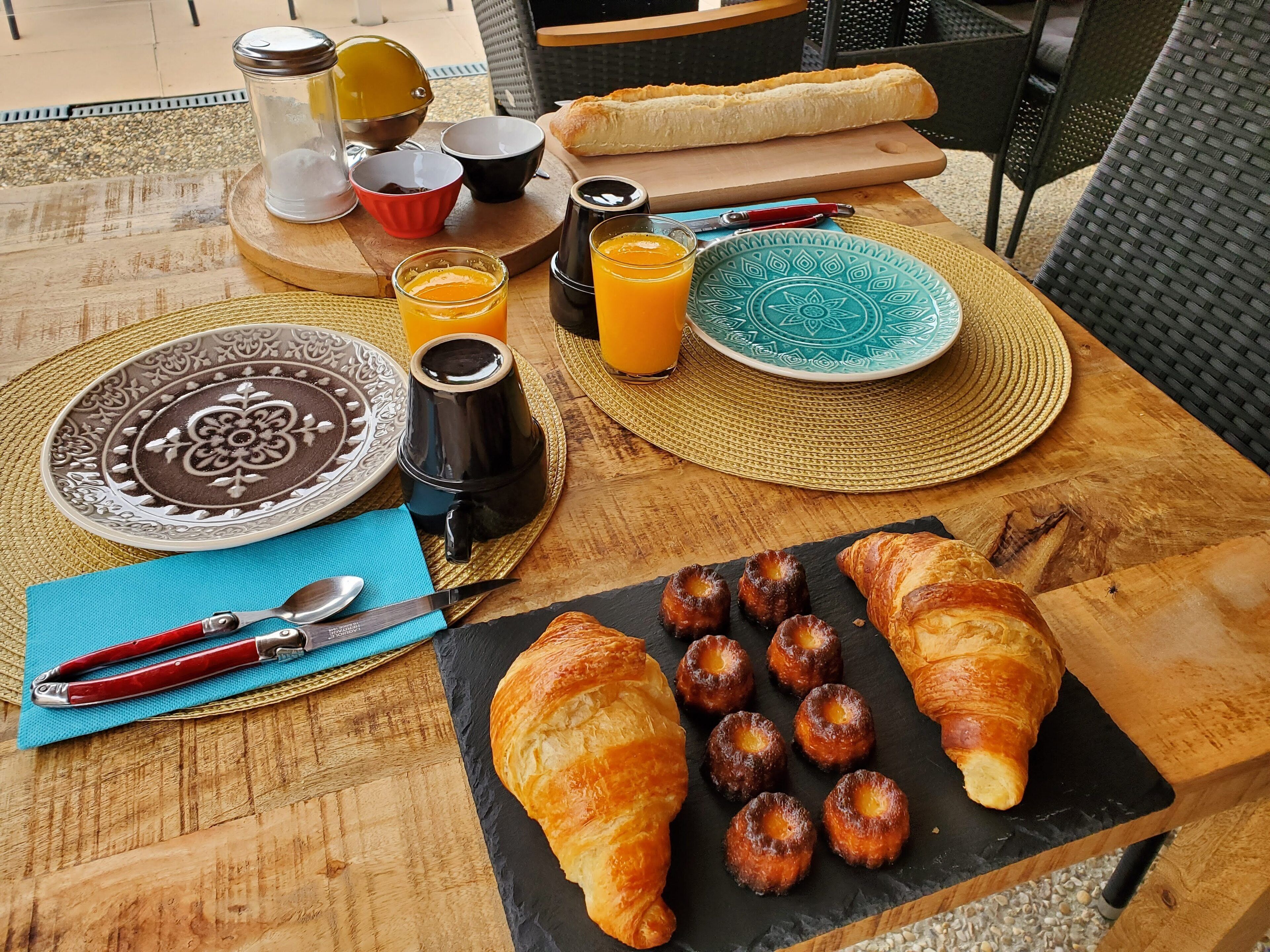 Una mesa de desayuno con croissants, bollería y zumo de naranja.