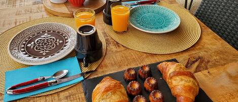 Una mesa de desayuno con croissants, bollería y zumo de naranja.