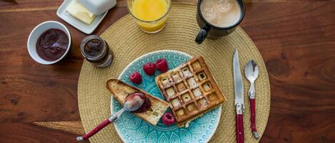 Desayuno con gofres, frambuesas y una taza de café sobre una mesa de madera.