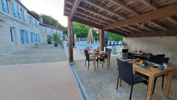 An outdoor patio area with a pool, a table with chairs, and a barbecue setup.