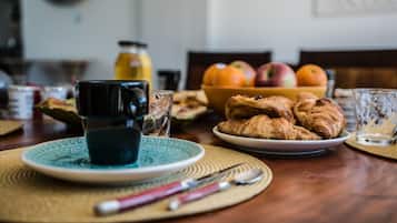 Une table en bois dressée pour le petit-déjeuner, avec des croissants, un saladier de fruits et une tasse de café.