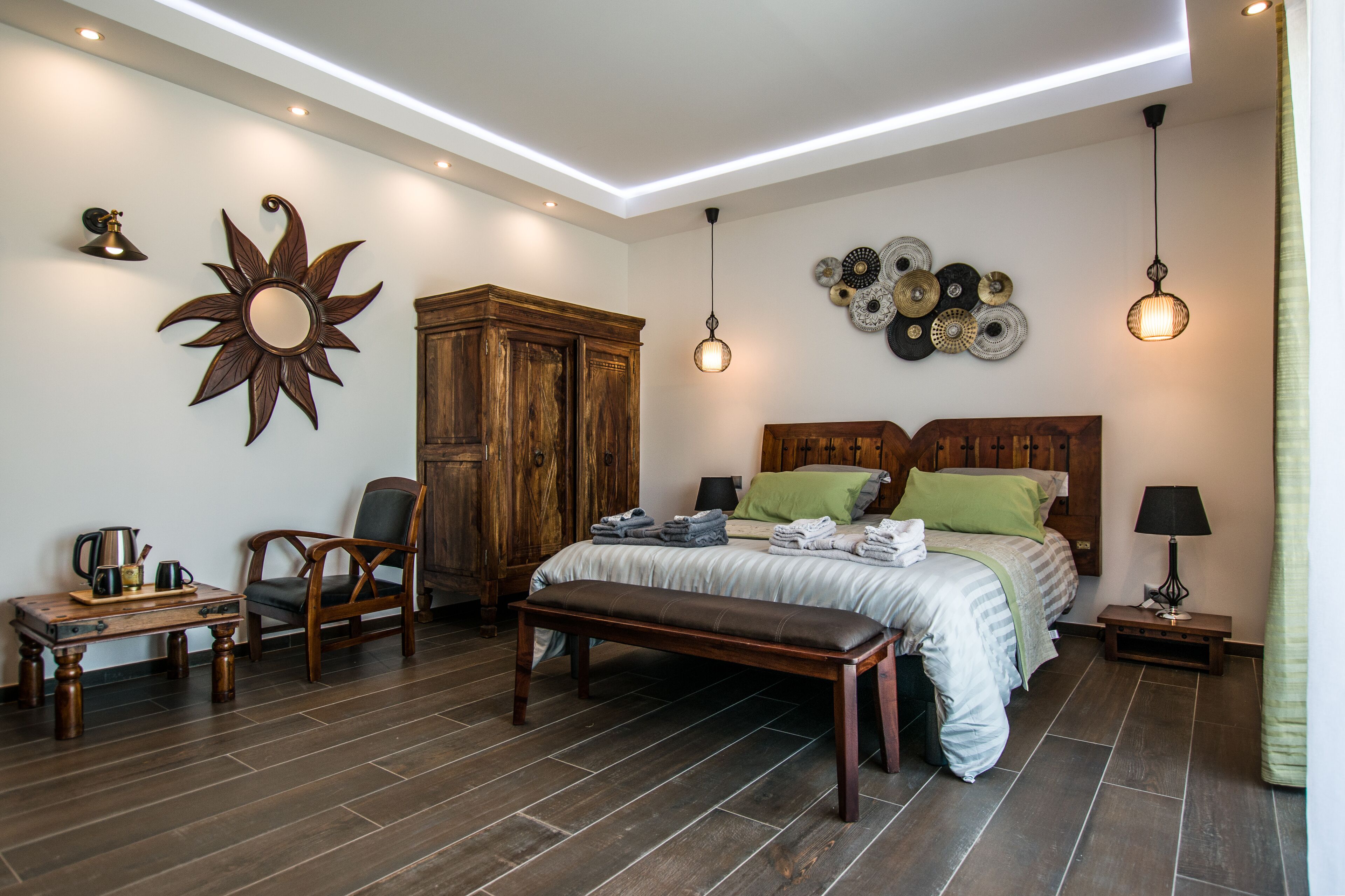 A bedroom with a wooden bed, a bench, a chair, a wooden cabinet, and a wall-mounted decorative item.