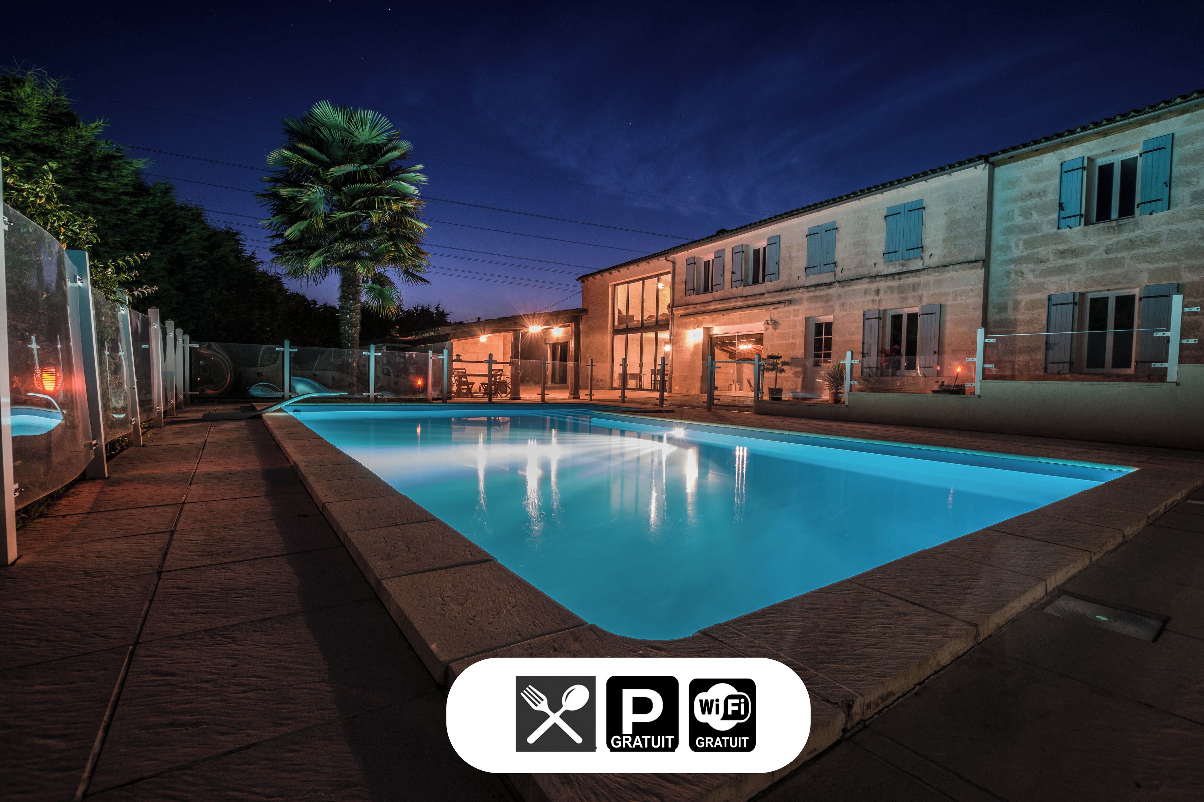Una piscina con solárium empedrado, una palmera y edificios con contraventanas azules.