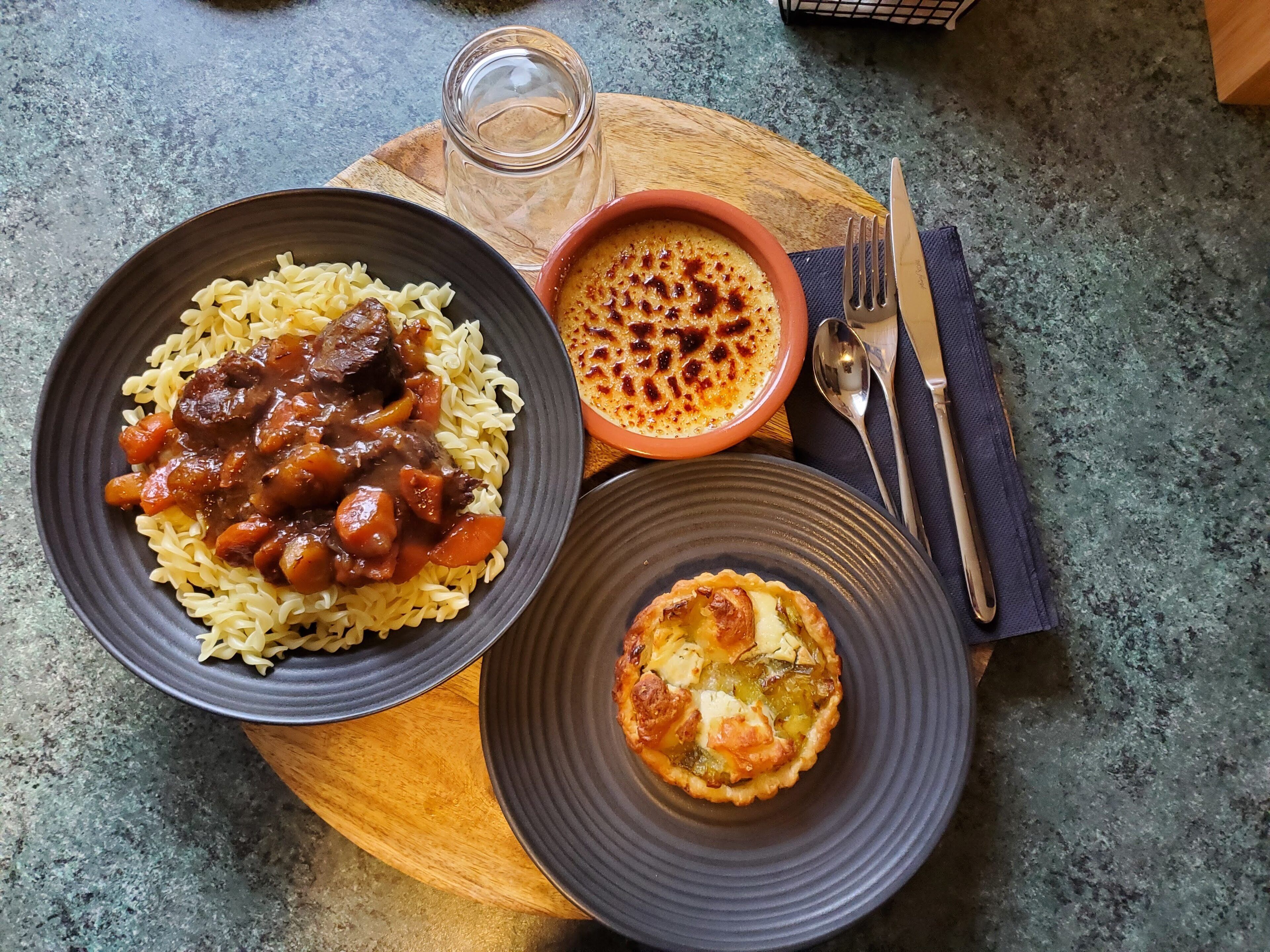 Pasta, una sopa en un tazón y una tarta sobre una tabla de madera.