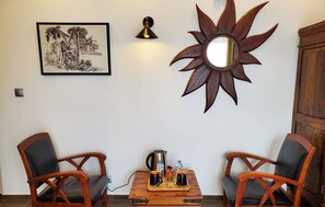 A dining area with two wooden chairs, a table with a coffee pot, a kettle, and condiments. A framed picture and a wall-mounted mirror are also visible. - Les Cuves (Chaniers)