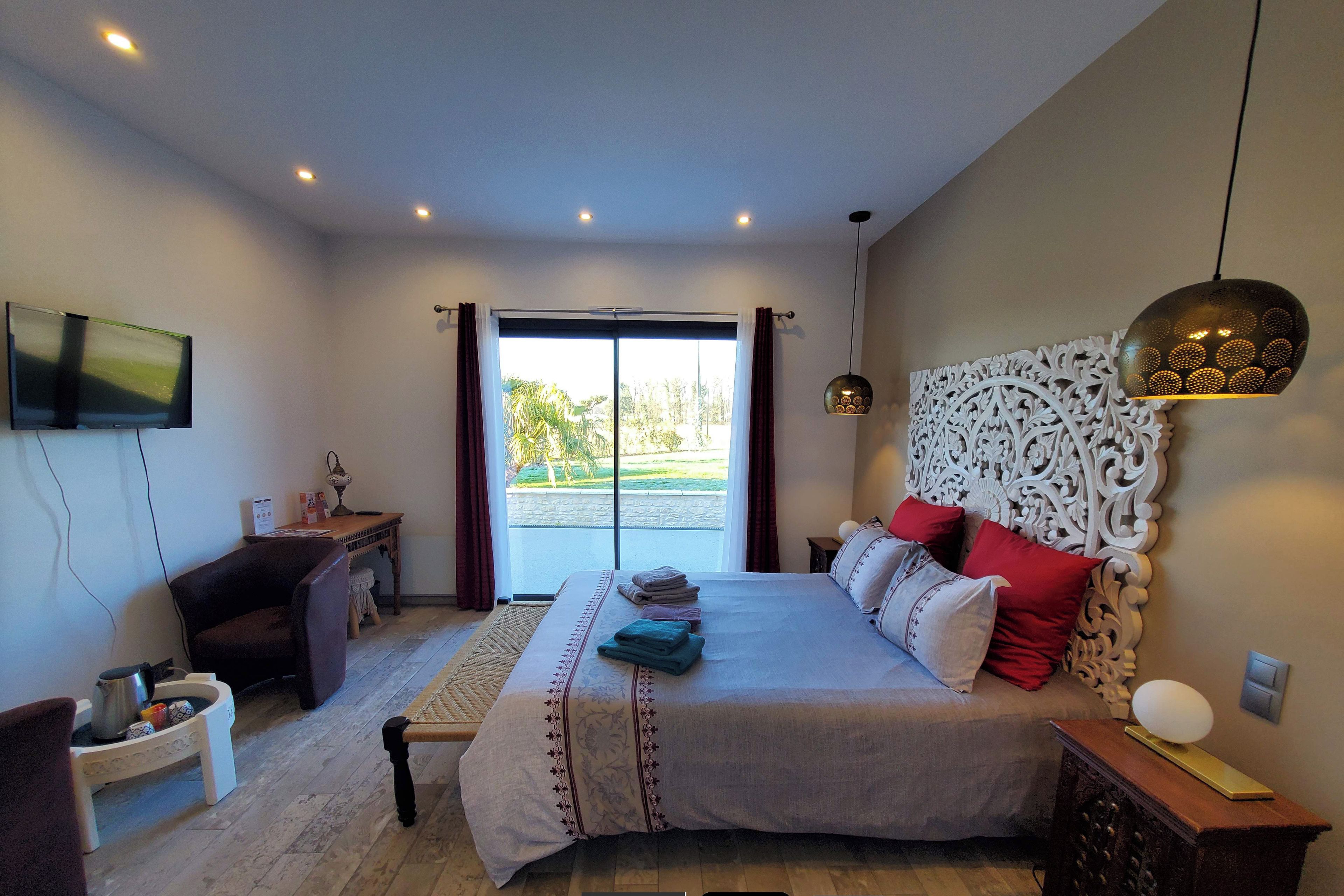 A bedroom with a large bed, a desk, a television, and a view of the outdoors.