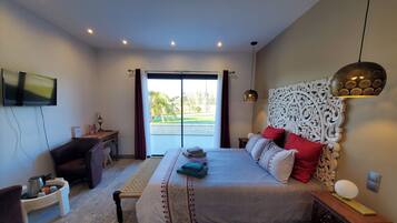 A bedroom with a large bed, a desk, a television, and a view of the outdoors.