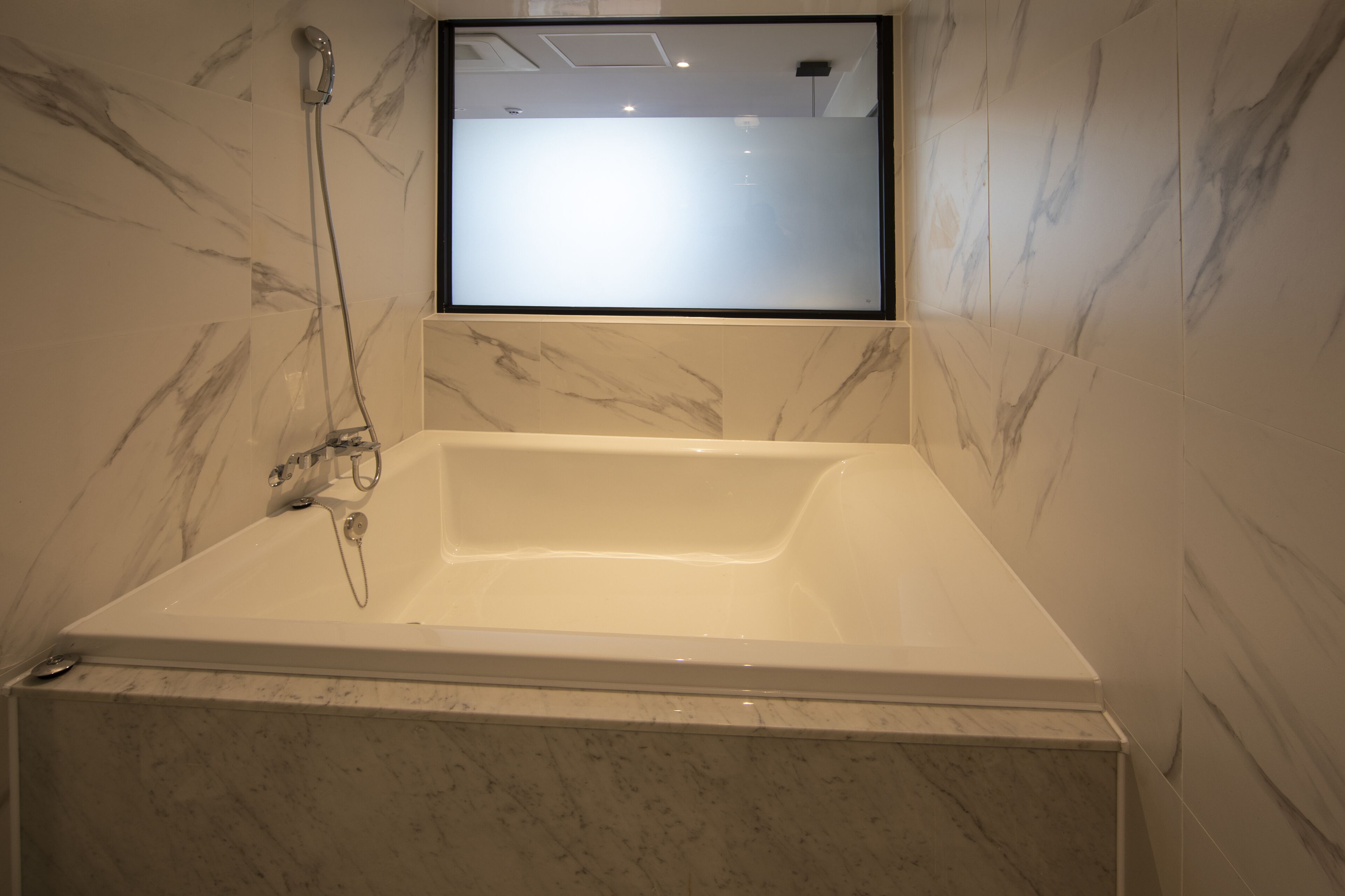 Een badkamer met een groot bad, een handdouche en een spiegel boven het bad.