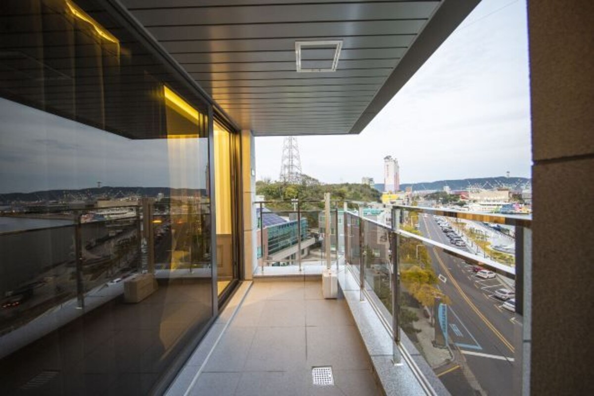 Un balcón con barandilla de vidrio, vista panorámica de la ciudad y un edificio de diseño moderno.