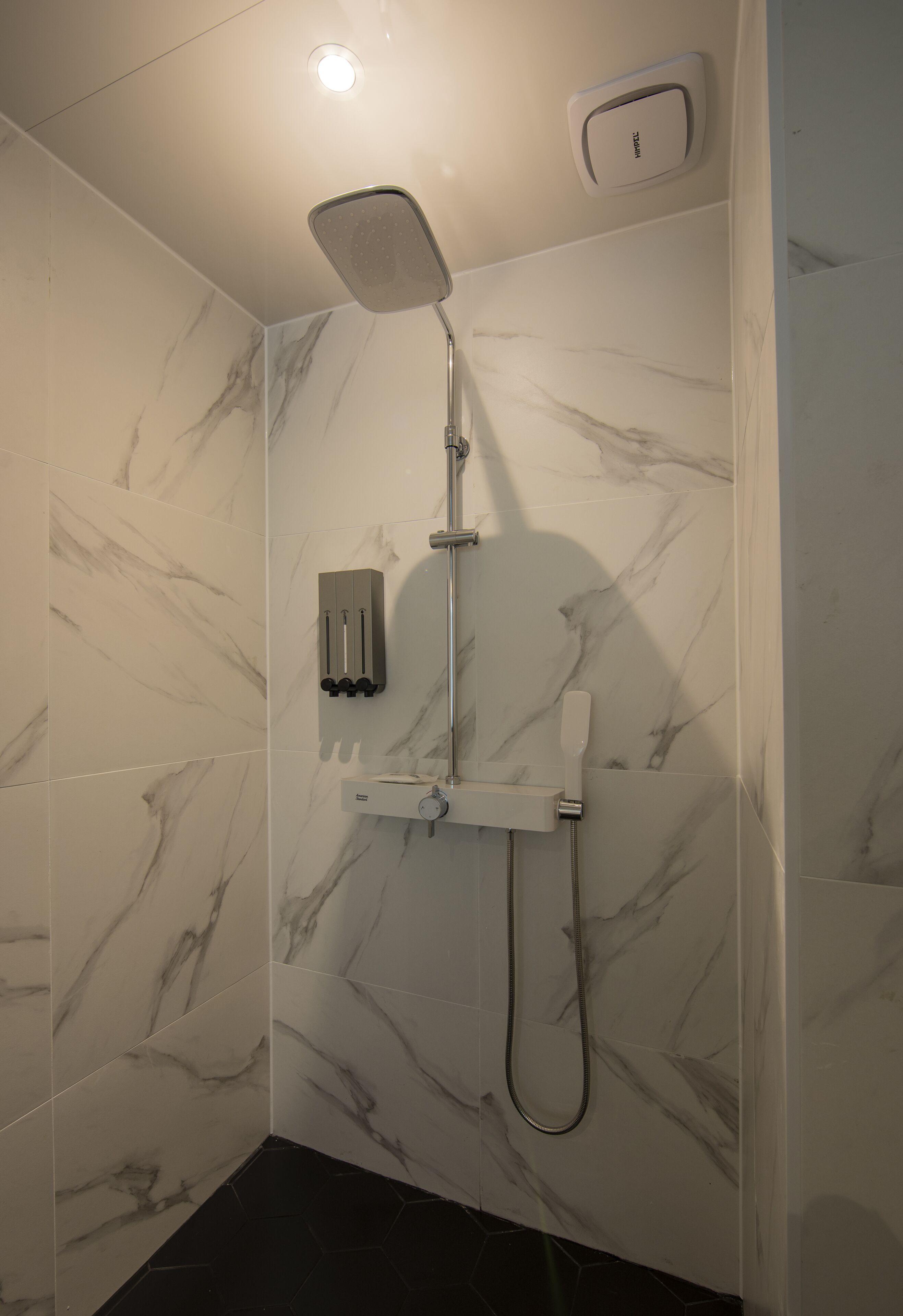 Une douche moderne dotée d’un pommeau de douche à main et d’un panneau de commande fixé au mur.