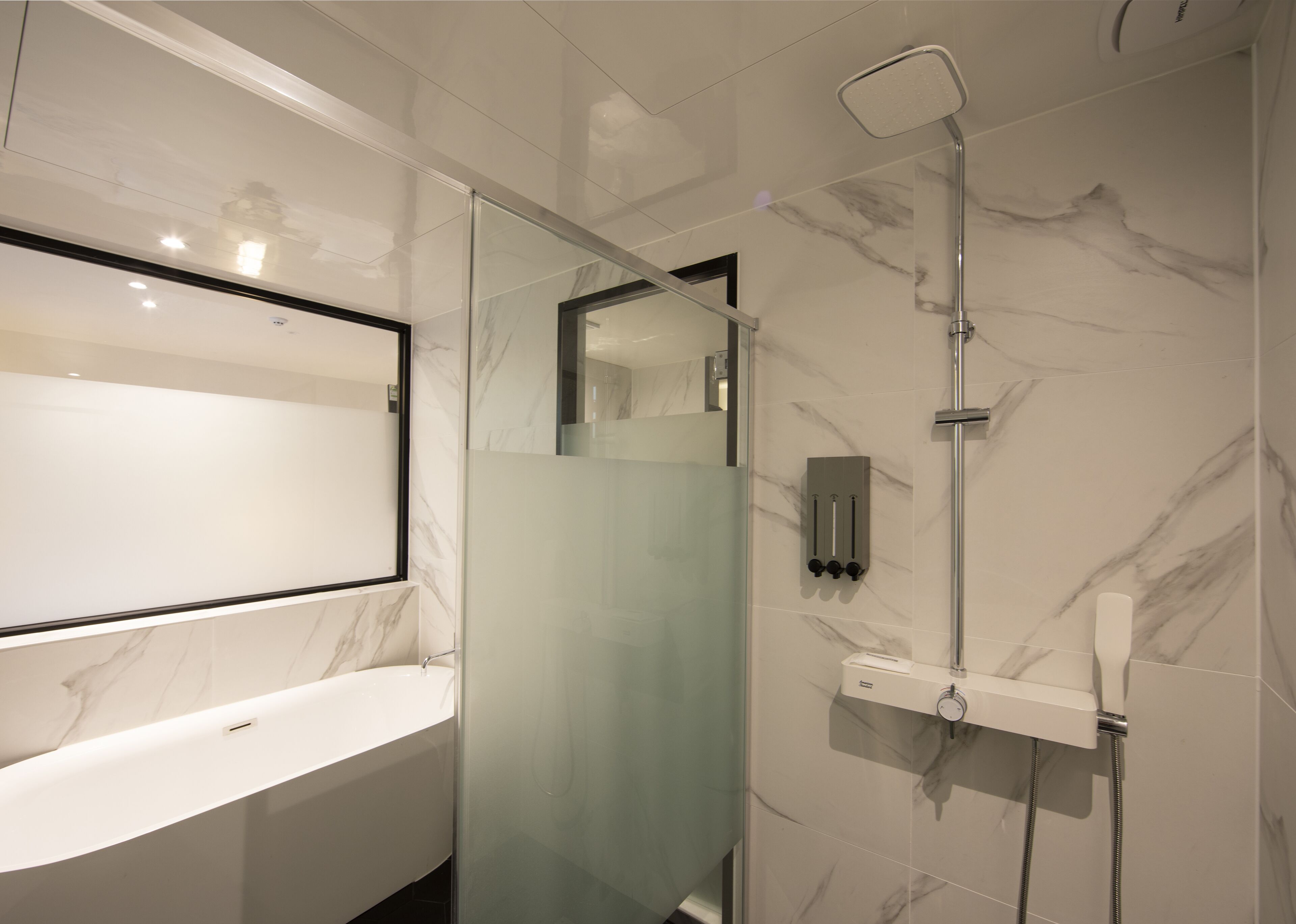Un baño moderno con ducha envuelta en vidrio, un espejo grande y un lavabo blanco.
