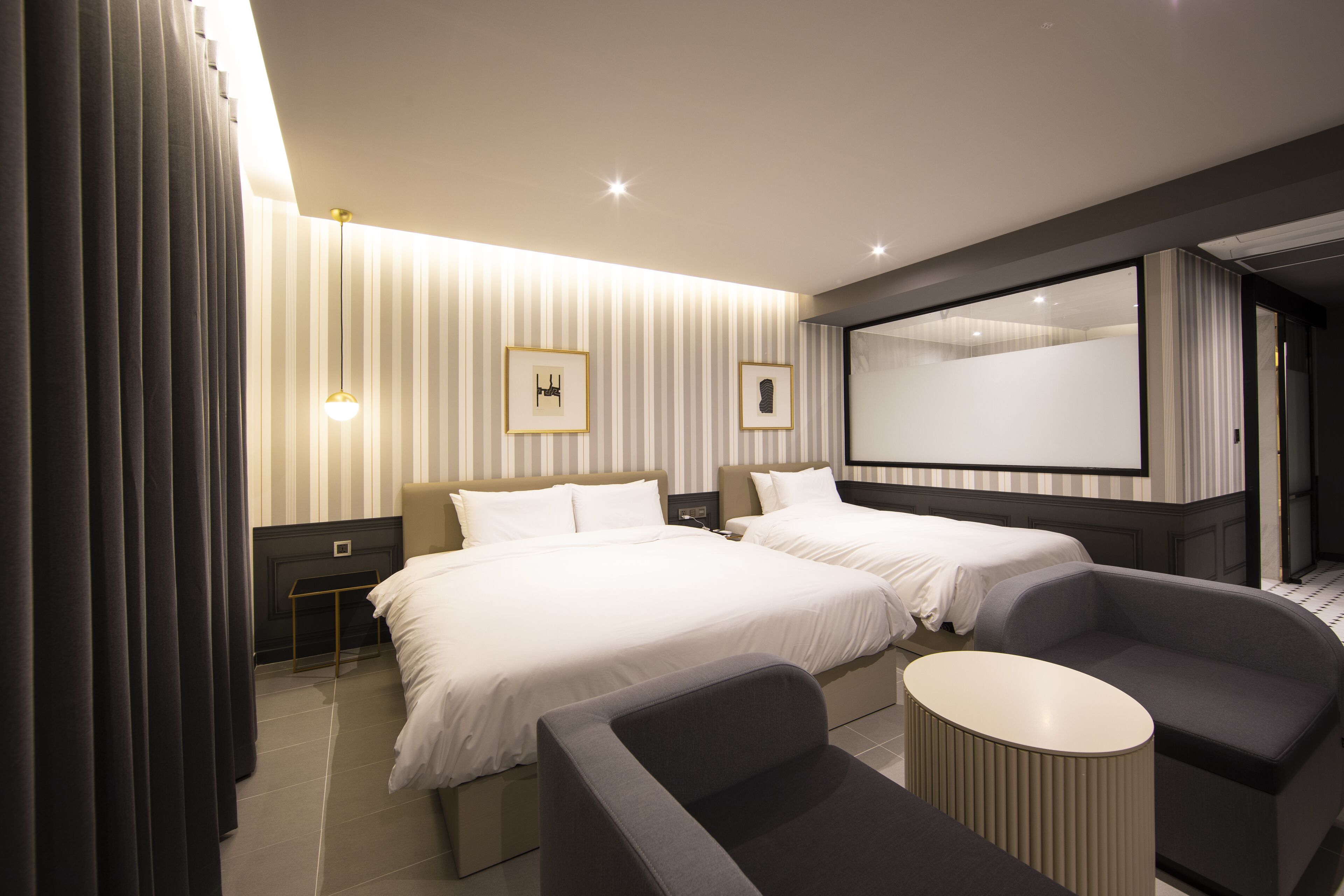 A modern hotel room with two beds, a seating area, a small table, and a large mirror.